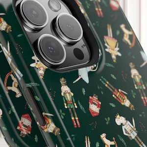 May include: Dark green phone case featuring a repeating pattern of festive Nutcracker-themed illustrations. The design includes toy soldiers, ballerinas, and other holiday figures. The case has a black border and a glossy finish.