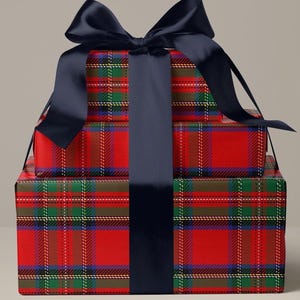 May include: Stacked gift boxes wrapped in red plaid paper with green, blue, and white accents. A large navy blue satin ribbon is tied in a bow on top, with a matching ribbon wrapping around the boxes. The boxes are a festive presentation.