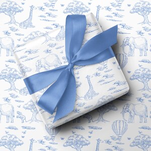 May include: A wrapped gift with a blue satin ribbon. The wrapping paper features a blue and white safari scene with elephants, giraffes, trees, hot air balloons, and butterflies. The gift is centered on a white background.