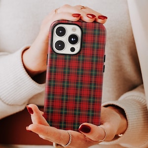May include: A red and green plaid phone case. The case has a classic tartan pattern. The phone case is held in a person's hands. The phone case has a camera module with three lenses.