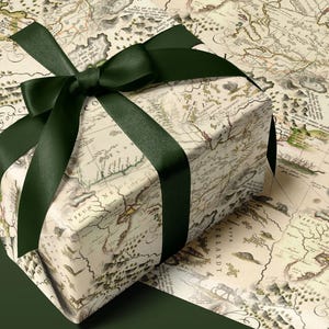 May include: A rectangular gift box wrapped in cream-colored paper featuring a vintage-style map print with black text and illustrations, tied with a dark forest green satin ribbon bow. The gift sits atop a matching dark forest green surface.