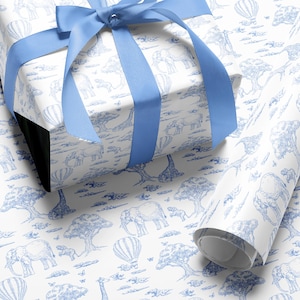 May include: A white gift box wrapped in paper with a blue safari animal print, tied with a blue satin ribbon. A roll of matching wrapping paper is visible in the foreground. The print features elephants, giraffes, trees, and hot air balloons.