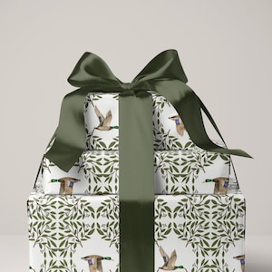 May include: A stack of wrapped gifts with a dark green satin bow. The wrapping paper features a white background with a repeating pattern of green leaves and flying ducks. The bow and ribbon are a solid dark green.