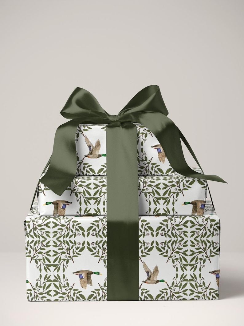 May include: A stack of wrapped gifts with a dark green satin bow. The wrapping paper features a white background with a repeating pattern of green leaves and flying ducks. The bow and ribbon are a solid dark green.