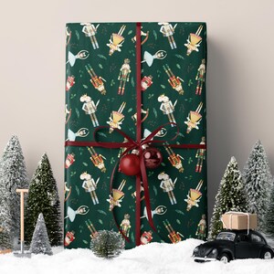 May include: A wrapped gift with a dark green background featuring a pattern of nutcracker soldiers. The gift is tied with a burgundy ribbon and a red ornament. Miniature Christmas trees and a toy car are in the foreground.