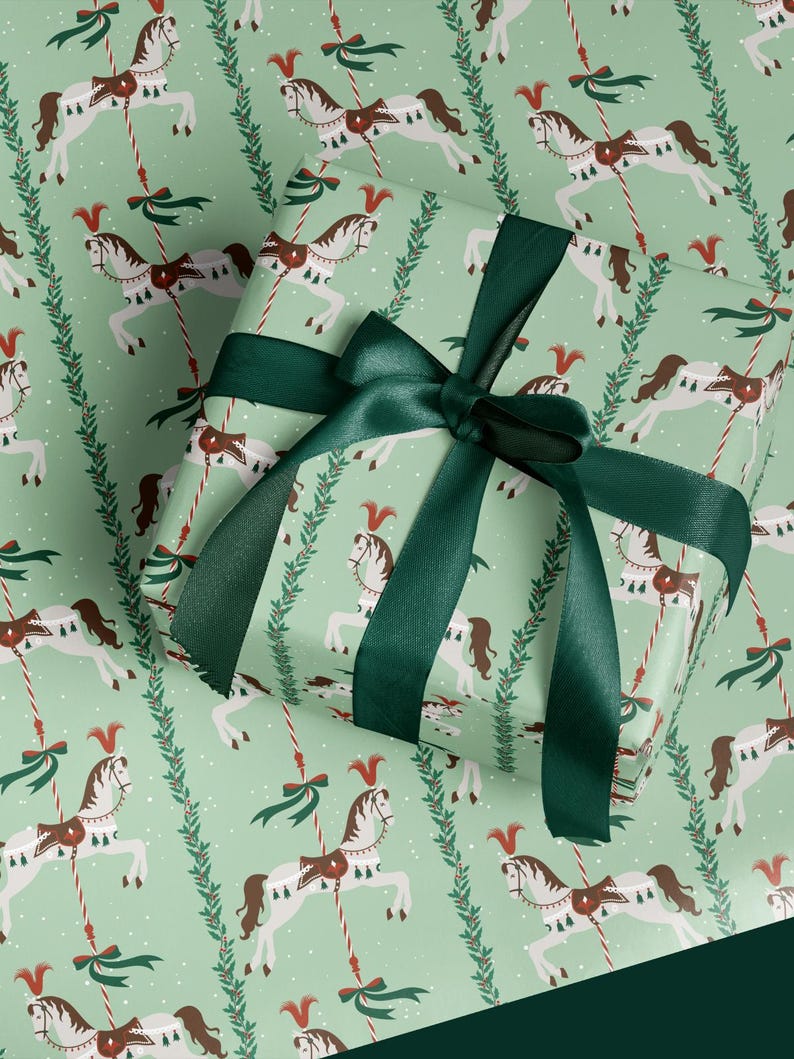 May include: Gift wrapped box with a green ribbon. The wrapping paper has a repeating pattern of white carousel horses with brown saddles and red accents on a light green background. Green sprigs and red and white striped poles are also featured.