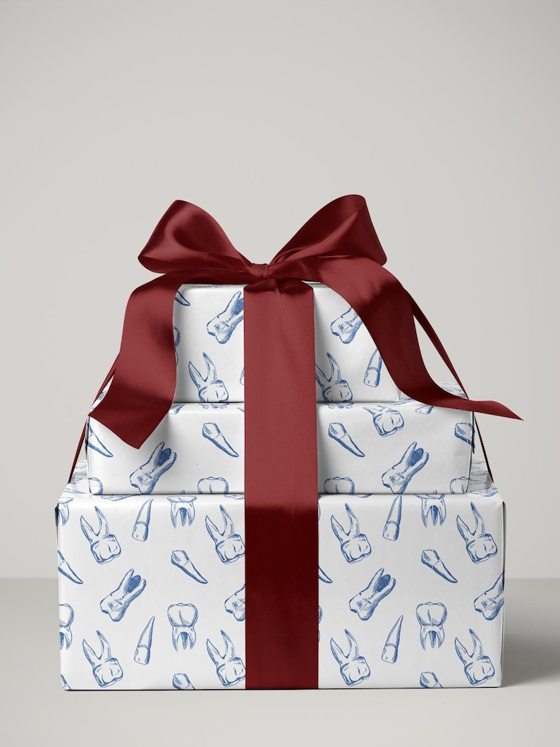 May include: Three stacked gift boxes wrapped in white paper with a blue tooth pattern. A wide, dark red satin ribbon and bow adorn the gifts. The dental-themed wrapping paper features various tooth illustrations.