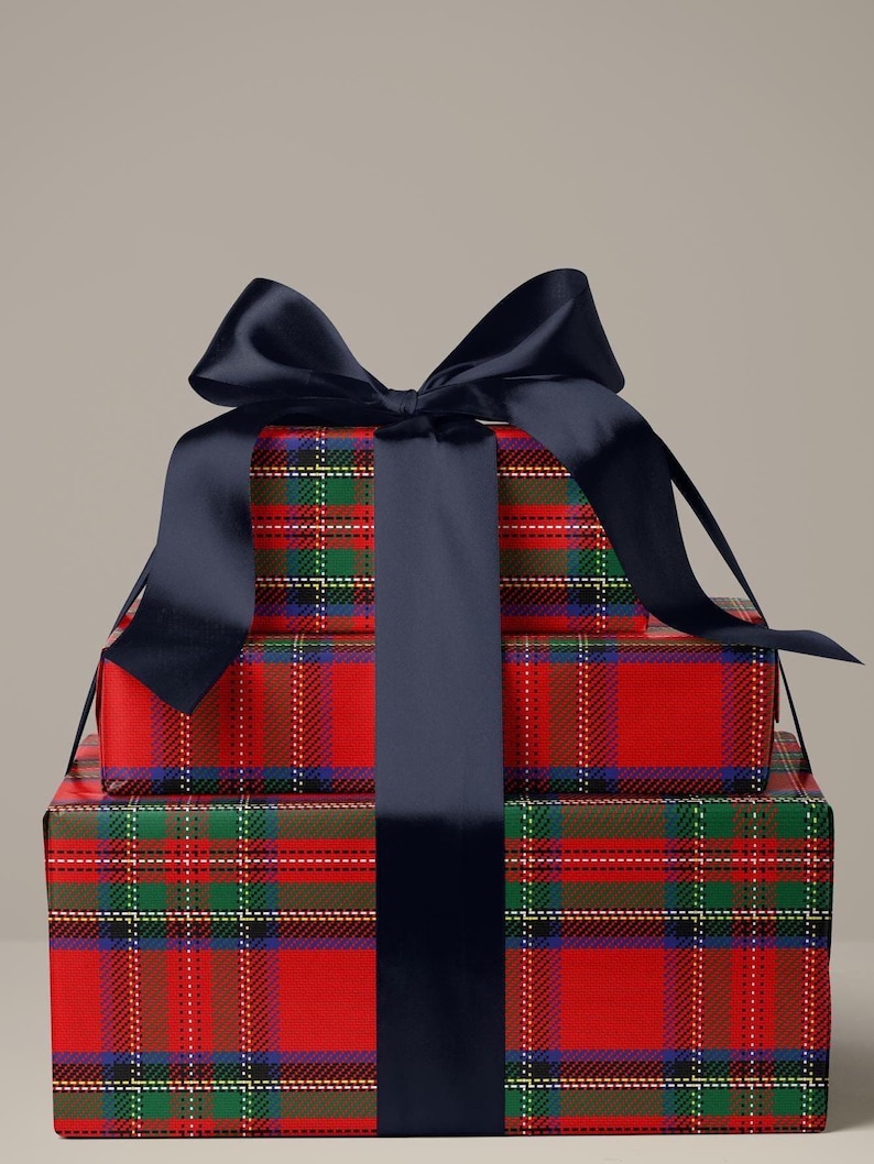 May include: Stacked gift boxes wrapped in red plaid paper with green, blue, and white accents. A large navy blue satin ribbon is tied in a bow on top, with a matching ribbon wrapping around the boxes. The boxes are a festive presentation.