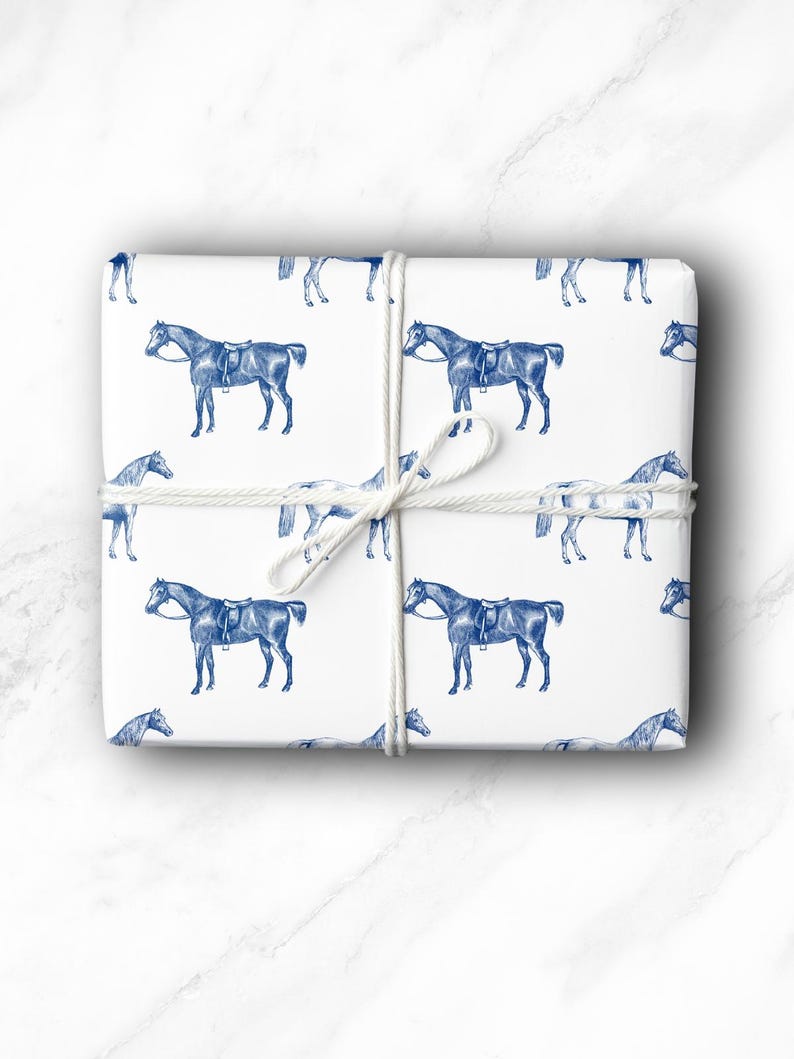 May include: White gift wrap featuring a repeating pattern of blue horse illustrations. The wrapped package is tied with white twine. The horses are depicted with saddles and bridles, creating a classic equestrian theme.