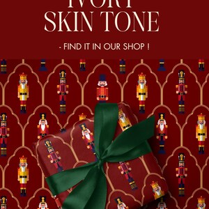 May include: A wrapped gift with a dark red background featuring a pattern of nutcracker soldiers. The gift is tied with a green ribbon. The text "ALSO AVAILABLE WITH IVORY SKIN TONE - FIND IT IN OUR SHOP!" is at the top.