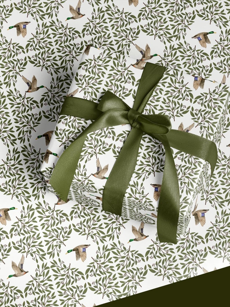 May include: A wrapped gift with a green satin ribbon bow. The wrapping paper features a repeating pattern of flying ducks and green leaves on a white background. The bow is a deep olive green.