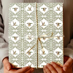 May include: A wrapped gift box featuring a repeating pattern of flying ducks and green foliage on a cream background. The box is tied with white twine. The overall theme is nature and wildlife.