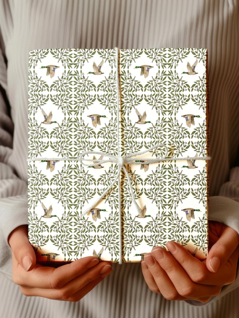 May include: A wrapped gift box featuring a repeating pattern of flying ducks and green foliage on a cream background. The box is tied with white twine. The overall theme is nature and wildlife.