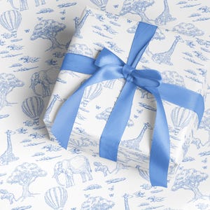 May include: A wrapped gift with white paper featuring a blue safari animal print, including elephants, giraffes, and hot air balloons. The gift is tied with a wide blue satin ribbon, forming a bow on top.