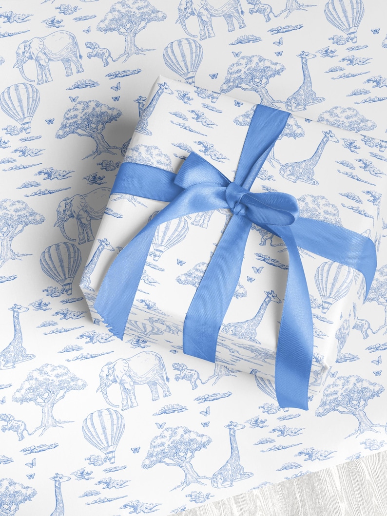 May include: A wrapped gift with white paper featuring a blue safari animal print, including elephants, giraffes, and hot air balloons. The gift is tied with a wide blue satin ribbon, forming a bow on top.
