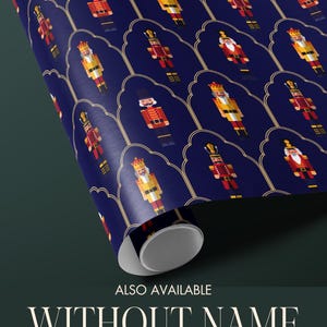May include: A roll of wrapping paper with a repeating pattern of pixelated nutcracker soldiers in red, yellow, and gold on a dark blue background. The text "ALSO AVAILABLE WITHOUT NAME - PERSONALIZATION IS OPTIONAL" is visible.