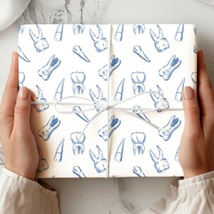 May include: A wrapped gift with a white background and a repeating pattern of blue teeth illustrations. The gift is tied with a white string. The overall theme is dental or medical.