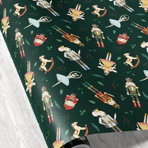 May include: Dark green wrapping paper with a repeating pattern of watercolor illustrations. The design includes nutcrackers, ballerinas, toy soldiers, toy mice, rocking horses, and small red gift boxes. The paper is rolled up, showing the pattern.