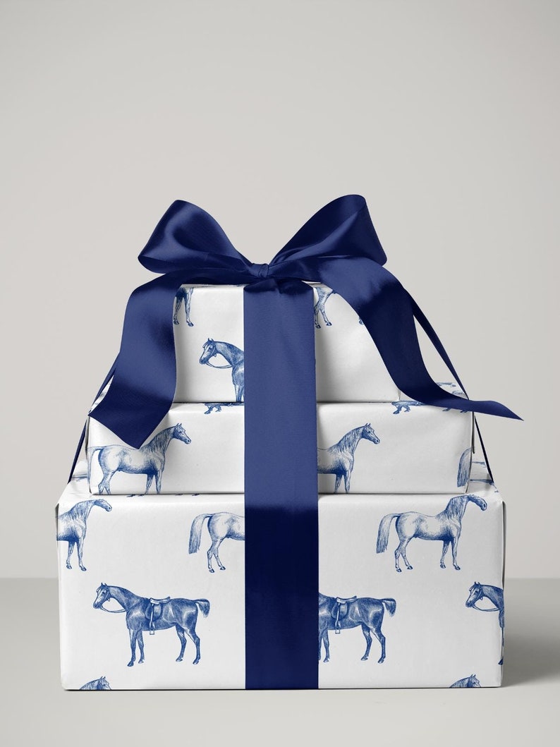 May include: A stack of wrapped gifts with a white background. The wrapping paper features a blue horse pattern. A large, dark blue satin ribbon and bow adorn the gifts. The gifts are stacked in a rectangular shape.