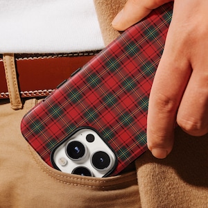 May include: A red, green, and black plaid phone case is partially visible in a pocket. The phone case has a black border and is held in a tan pocket. A brown belt and white shirt are also visible.