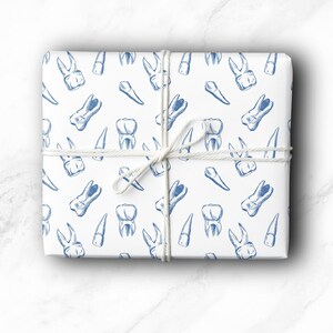 May include: A wrapped gift with white paper featuring a blue illustration of teeth. The gift is tied with white twine. The teeth illustrations include molars, incisors, and premolars.