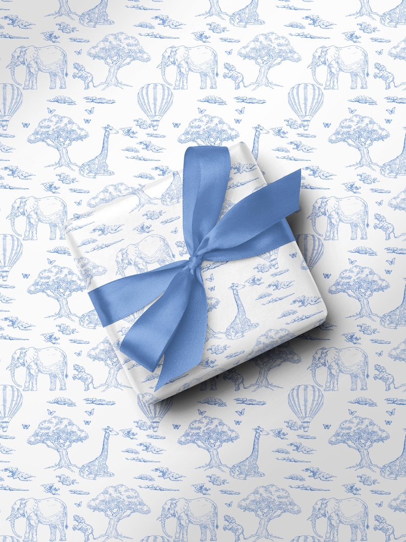 May include: A wrapped gift with a blue satin ribbon. The wrapping paper features a blue and white safari scene with elephants, giraffes, trees, hot air balloons, and butterflies. The gift is centered on a white background.