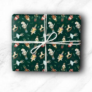 May include: A wrapped gift with a festive green paper featuring a repeating pattern of nutcrackers, rocking horses, ballerinas, and other holiday-themed illustrations. The gift is tied with white twine.