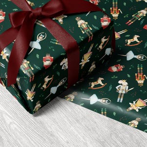 May include: A wrapped gift with a burgundy bow sits on a white wood-grain surface. The wrapping paper is dark green with a repeating pattern of nutcrackers, ballerinas, and toy soldiers. The bow is made of a wide, satin ribbon.