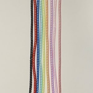May include: A collection of colorful beaded chains in a rainbow of hues, including black, red, blue, green, yellow, orange, purple, pink, and rose gold. The chains are displayed vertically against a white background.