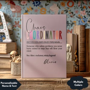 May include: A personalized notebook with the text "Chaos Coordinator" in colorful letters. The definition of the term is printed below, along with the name "Olivia". The notebook is light pink and has a hardcover.