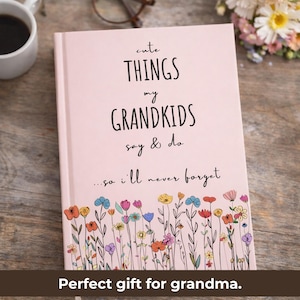 May include: A pink journal with the text "cute THINGS my GRANDKIDS say & do...so I'll never forget." The bottom of the journal features a colorful floral design. A cup of coffee and glasses are in the background.