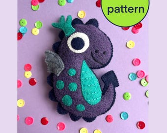 May include: A purple felt dragon with teal and white accents, surrounded by colorful sequins. The dragon has a friendly expression and a crown. A green circle with the text "PDF pattern" is in the upper right corner.