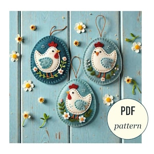 May include: Three felt Easter egg ornaments with chicken designs. Each egg is a teal color with a white chicken, red comb, and floral accents. The ornaments have brown string hangers and are on a light blue wooden surface. The image also includes small white and yellow flowers.