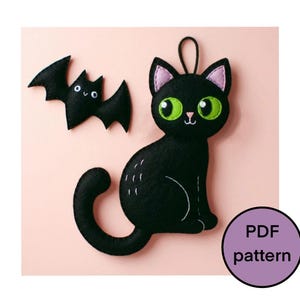 May include: Black felt cat and bat ornaments with green eyes and pink accents. The cat has a curved tail and white details. The bat has small white eyes. A purple circle with the text "PDF pattern" is in the lower right corner.