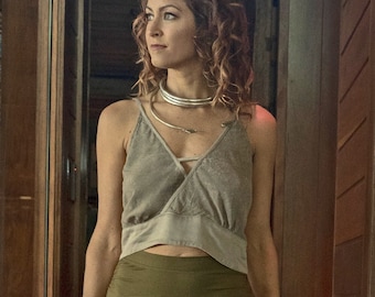 May include: A woman wearing a silver necklace and a gold cuff bracelet. She is wearing a light gray top and an olive green skirt. The top has a crisscross design. The skirt is a wrap style.