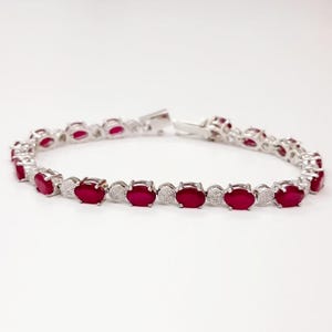 May include: A silver bracelet with a row of oval-shaped red gemstones and smaller clear gemstones.