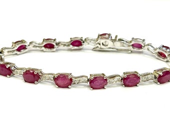 May include: A silver bracelet with a row of oval-shaped ruby gemstones and small diamonds set in the metal.