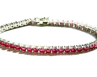 May include: A silver tennis bracelet with a row of round, red ruby stones.