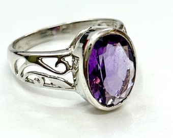 May include: A silver ring with an oval-shaped amethyst gemstone. The ring has a delicate, filigree design.