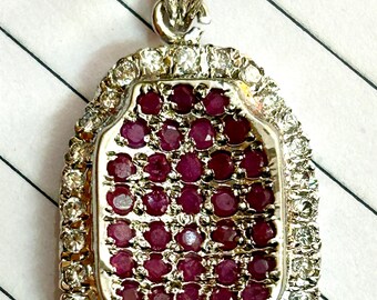 Op de afbeelding: Een zilveren hanger met een rode robijn, omringd door een halo van kleinere diamanten.