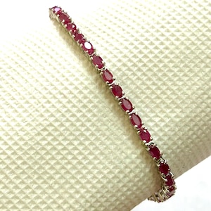 Pode incluir: Um bracelete de ténis de prata com pedras preciosas vermelhas de forma oval.