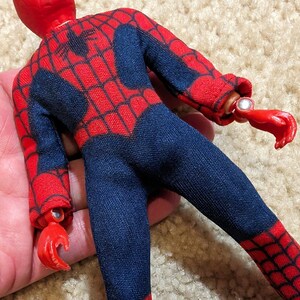 Peut inclure: Une figurine d'action de Spider-Man rouge et bleue. La figurine a un motif de toile d'araign&eacute;e sur le costume et une t&ecirc;te rouge.
