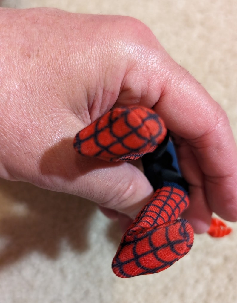 Peut inclure: Un jouet en peluche rouge et bleu en forme de Spiderman. Le jouet a un motif de toile d'araign&eacute;e sur les bras et les jambes.