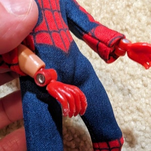 Peut inclure: Une figurine d'action rouge et bleue avec un motif de toile d'araign&eacute;e rouge sur la poitrine. La figurine a un bras et une main amovibles.