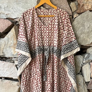 May include: A long, flowing, red and white cotton kaftan with black trim. The kaftan has a V-neck and a tie at the waist.