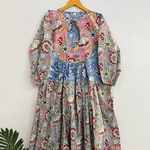 Könnte beinhalten: Ein langes, mehrschichtiges Blumenkleid mit einem Schlüssellochausschnitt und langen Ärmeln. Das Kleid ist aus Baumwolle und hat ein Patchwork-Design mit rosa, blauen und grauen Blumenmustern.