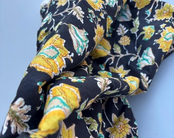 May include: Black fabric with a yellow and green floral print. The fabric is folded and bunched up.