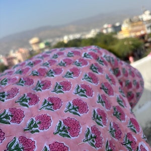 Puede incluir: Una tela rosa con un patrón floral de pequeñas flores rosas con tallos verdes. La tela está doblada y el fondo está desenfocado.