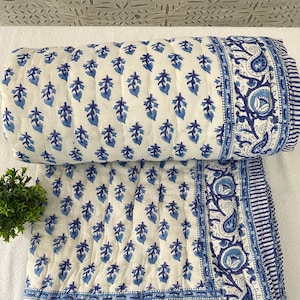 May include: A white cotton quilt with a blue floral pattern. The quilt has a border of paisley designs and a striped border.