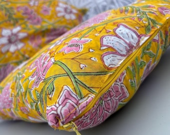 May include: Two decorative throw pillows with a vibrant floral pattern. The pillows feature a bright yellow background with pink and white flower designs and green stems. A yellow zipper is visible on the side of one pillow.